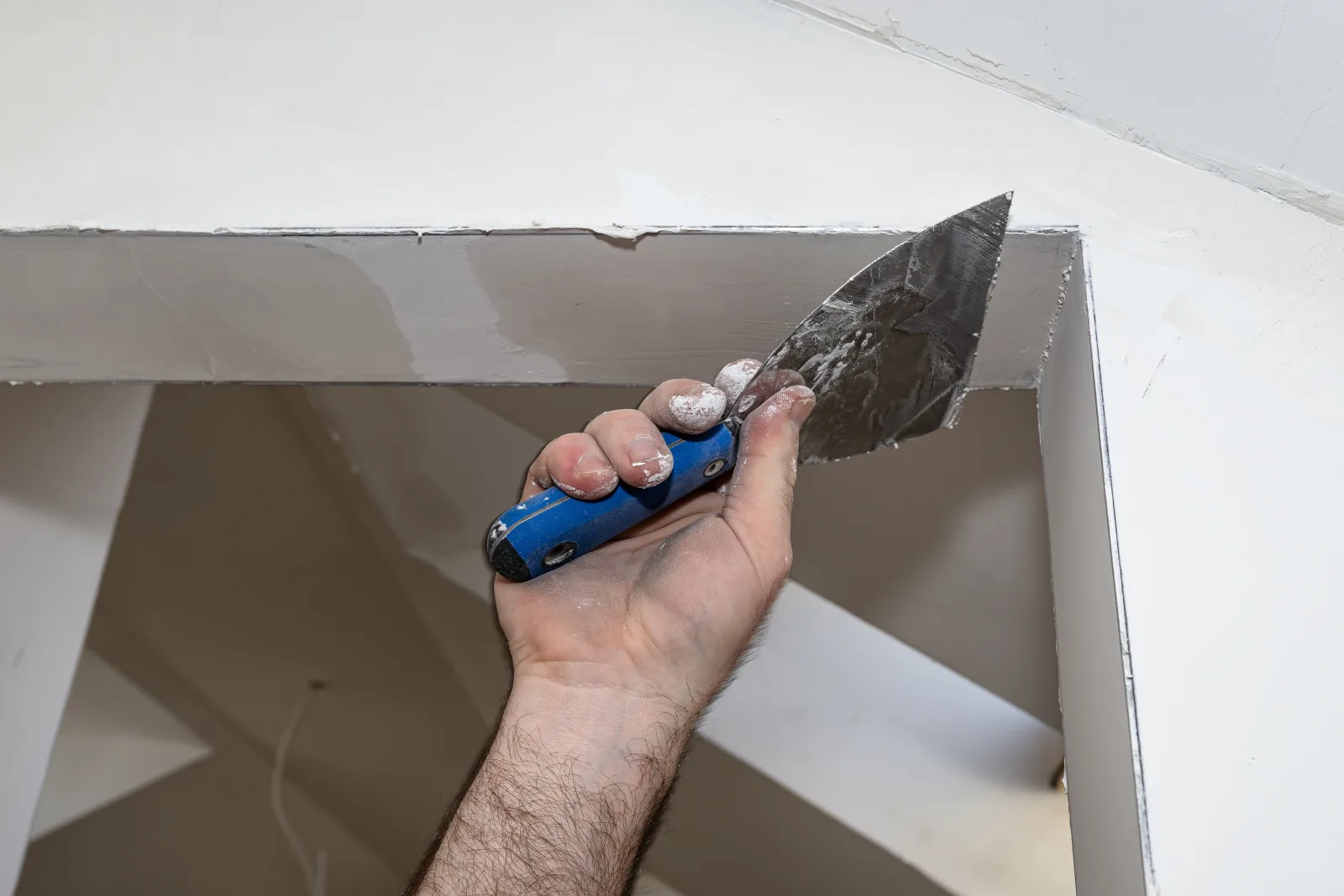 A hand drawing jointing compound along a drywall angle with a broad knife, plaster dust dried on the fingers — fix and flip insurance in Arizona