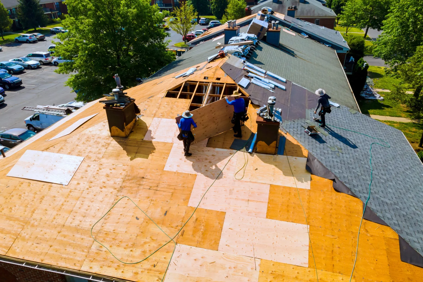 Roofers stripping a wide residential roof back to its plywood deck, one bay open to the rafters and the old shingles peeled away at the ridge — fix and flip insurance in Texas