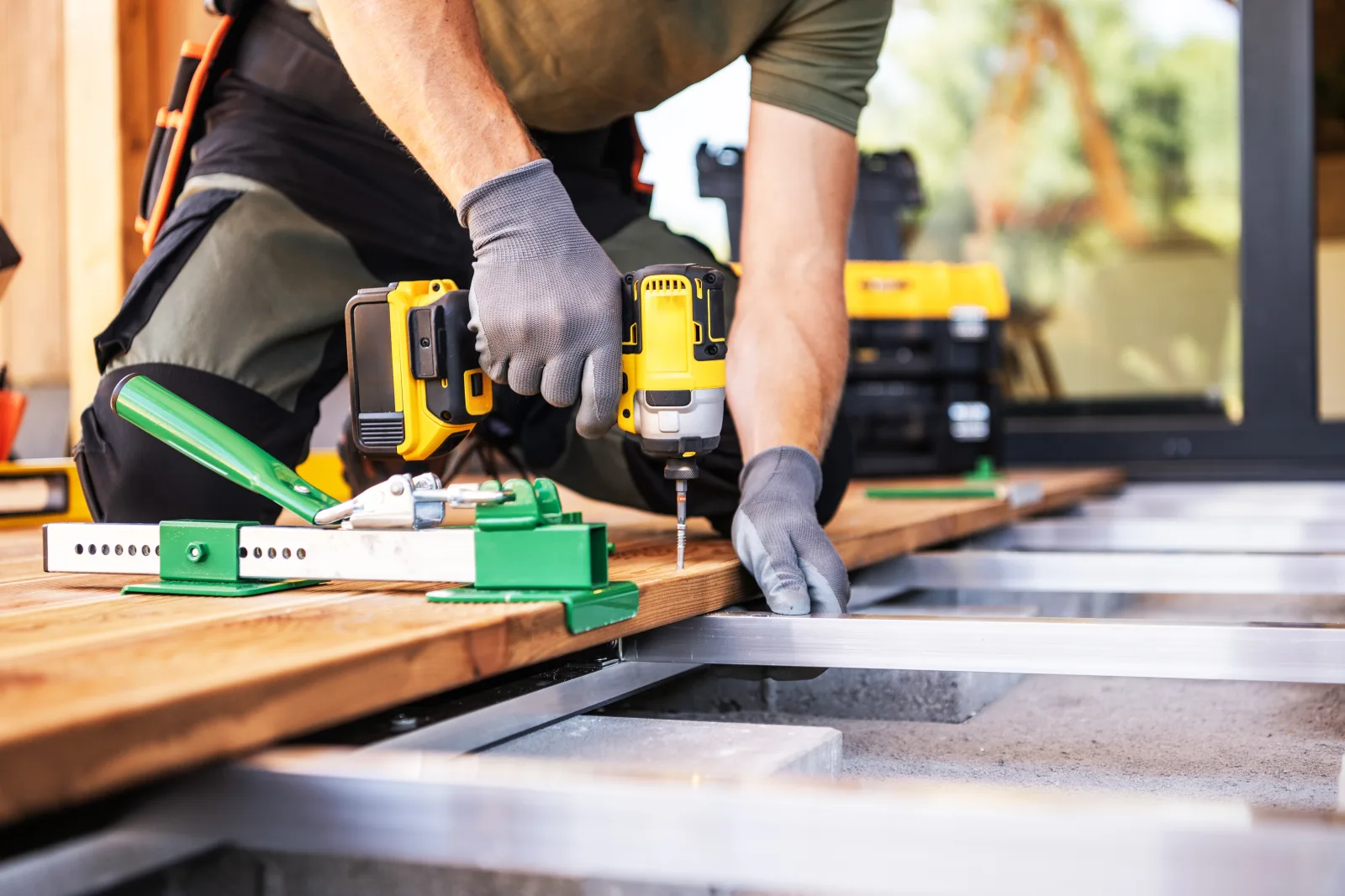 A gloved worker driving a screw into a hardwood deck board with a cordless impact driver, spacing jigs set along the joists — fix and flip insurance in West Virginia