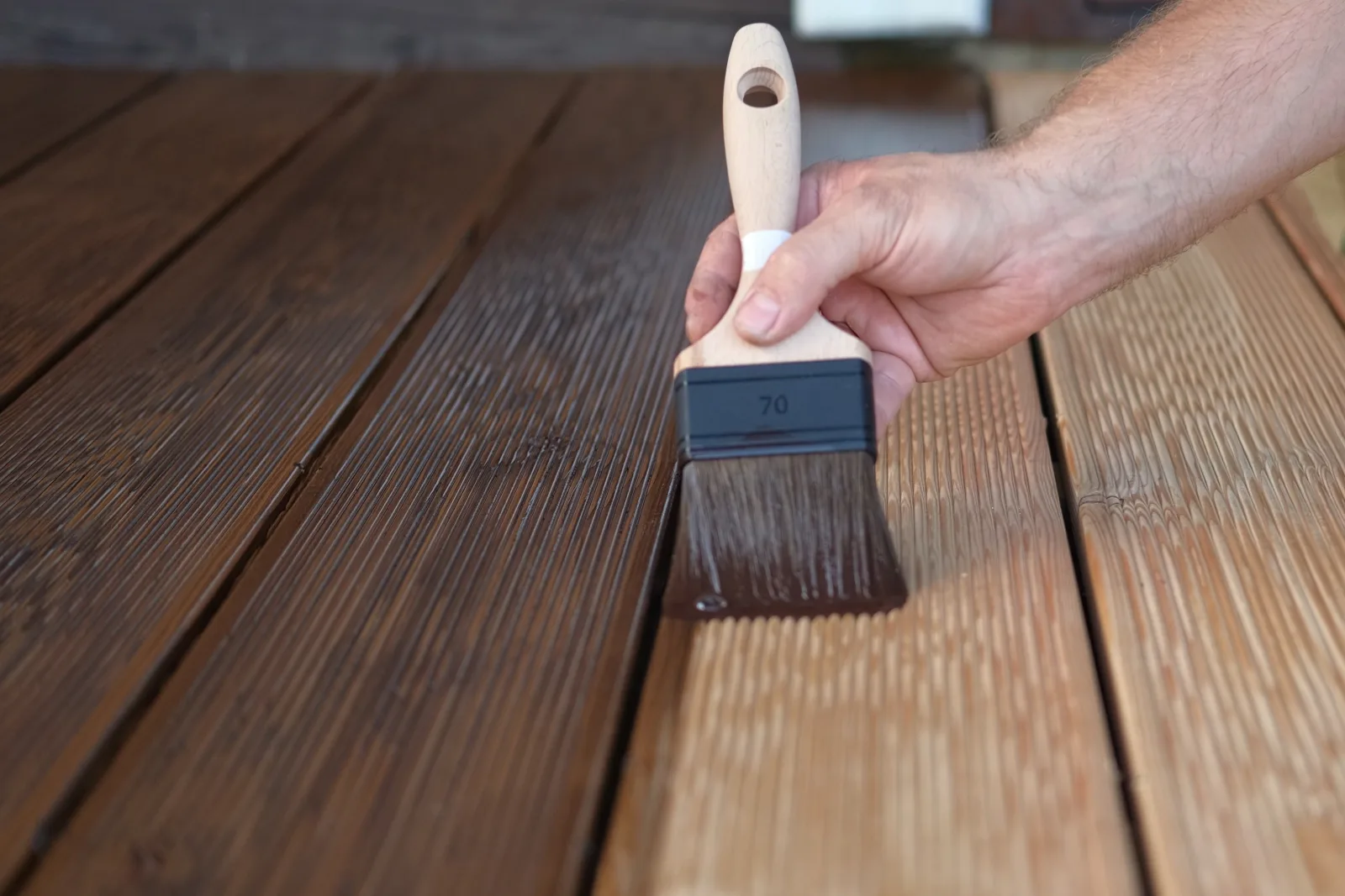 A brush pulling dark stain along ribbed decking, the boards already coated running darker than the raw timber alongside — fix and flip insurance in Connecticut
